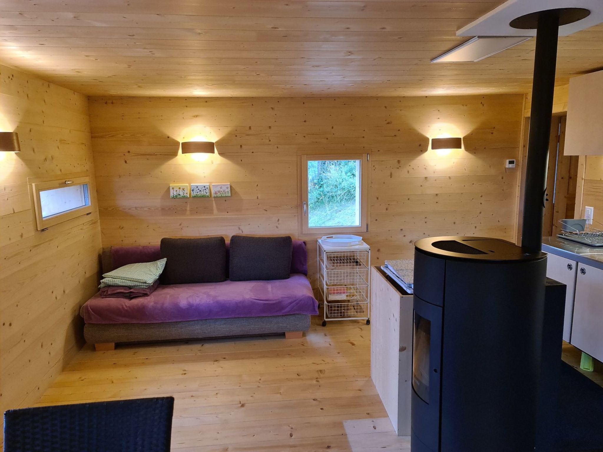 Een gezellig chalet interieur met een bank, een houtkachel en een raam.