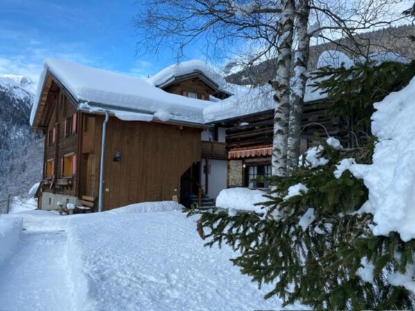 Una cabaña de madera con techo nevado, rodeada de nieve y árboles.