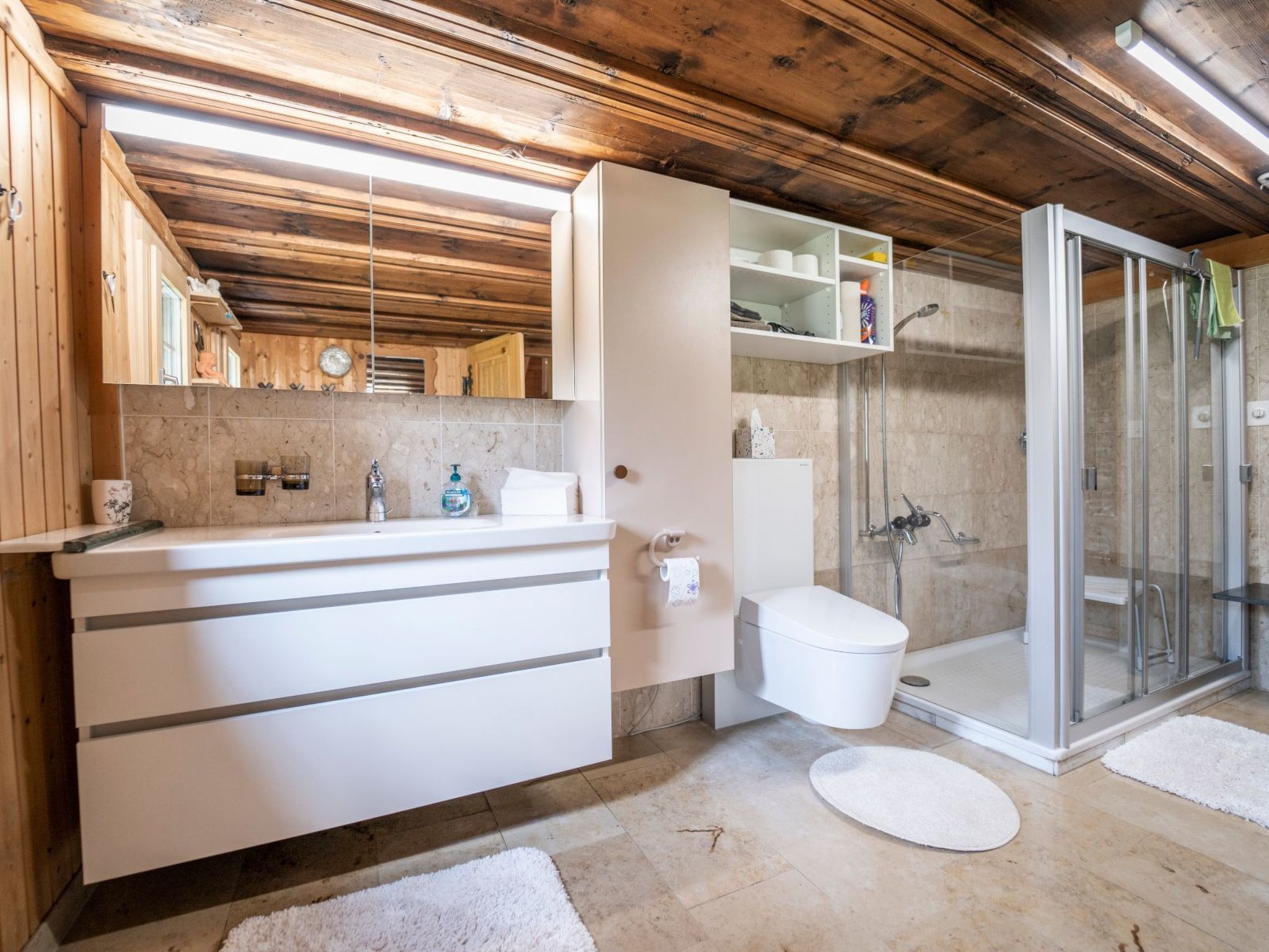 Een badkamer met een houten plafond, een witte wastafel, toilet en een douchecabine met glazen wanden.