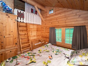 Una habitación tipo cabaña de madera con una cama, una escalera, un ventanal y un balcón pequeño.