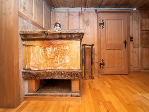 Un interior de madera con chimenea de piedra, una puerta con picaporte negro y una mesa de vidrio.
