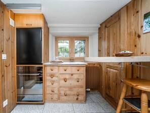 Cocina compacta con armarios de madera, horno integrado y ventana con vista a vegetación.
