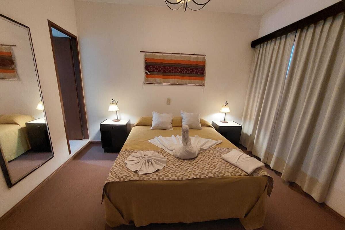 A hotel room with a large bed, two bedside tables with lamps, a mirror, and a window with curtains.