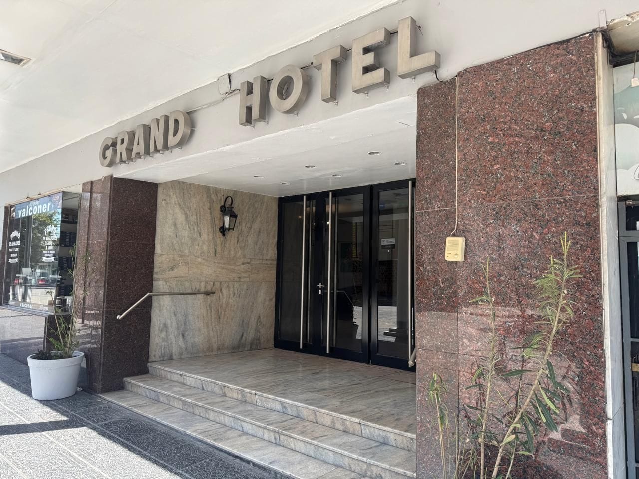 A hotel entrance with a marble facade, a glass door, and a sign that reads 'GRAND HOTEL.'