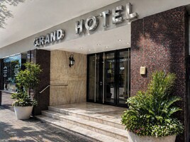 Fachada de hotel con un cartel imponente, una escalera y plantas en macetas.
