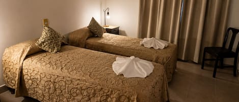 A hotel room with two beds, a chair, a nightstand, a wall hanging, and an air conditioning unit.