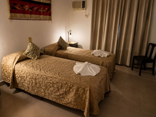 Habitación de hotel con dos camas, una silla, una mesita de noche, un cuadro en la pared y un equipo de aire acondicionado.