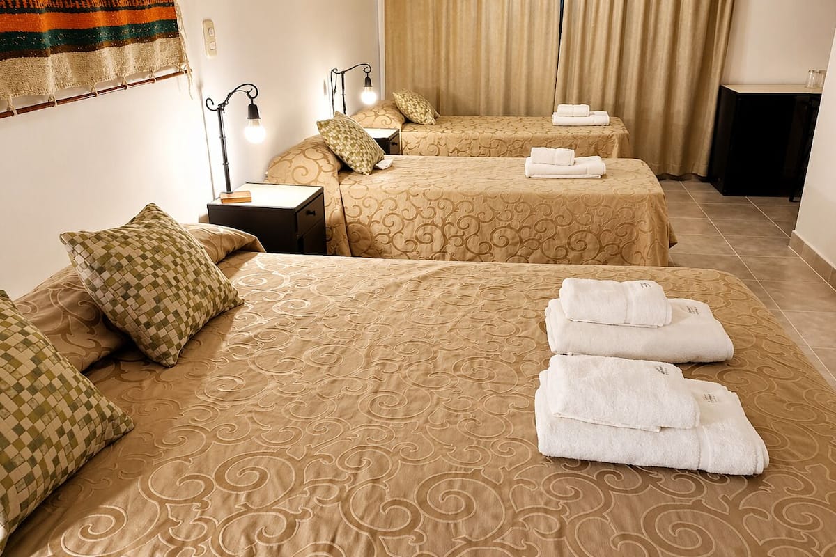 A hotel room with two beds, a nightstand, a lamp, and towels.