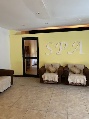 A reception area with a 'SPA' sign, two brown sofas with patterned cushions, and a tiled floor.
