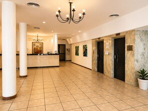 A hotel lobby with a reception desk, a chandelier, a digital clock, and a potted plant.