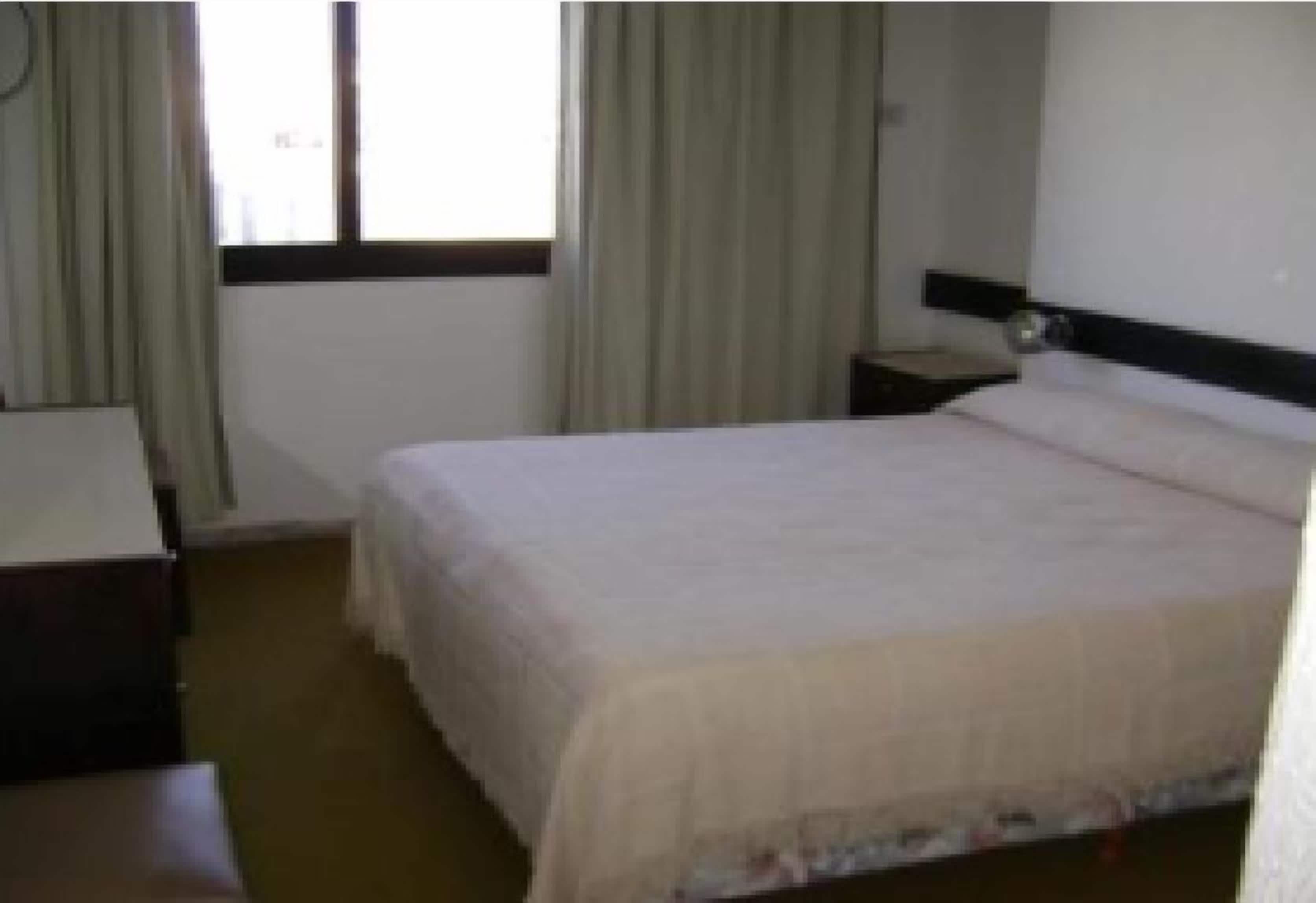 Habitación de hotel con cama, mesita de noche, escritorio y ventana con cortinas.