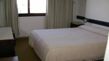 Habitación de hotel con cama, mesita de noche, escritorio y ventana con cortinas.