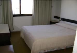 Habitación de hotel con cama, mesita de noche, escritorio y ventana con cortinas.