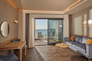 Et hotelværelse med balkon, sofa, spisebord og et spejl.