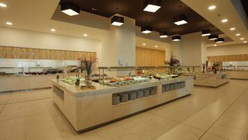 Amplia zona de buffet con múltiples estaciones de servicio, suelo de baldosas e iluminación colgante moderna.