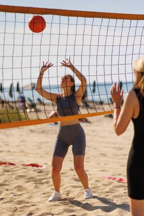 Partido de voleibol de playa con jugadores con ropa deportiva, una red de voleibol y una playa arenosa al fondo.