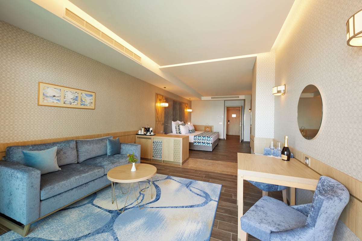Une chambre d’hôtel moderne avec un canapé, une petite table ronde, un lit avec une table de chevet et un miroir au mur.