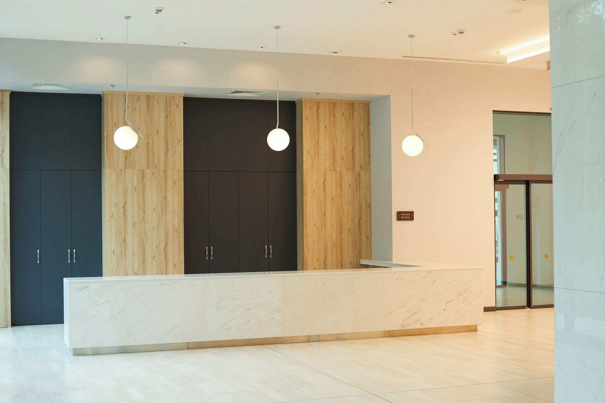 A reception desk with a marble top, wooden paneling, and pendant lighting.