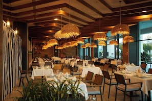 En restaurang med flera bord, hängande taklampor av rotting och utsikt genom stora fönster.