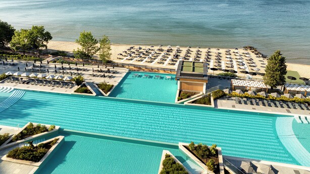 Un resort con una gran piscina, zona de playa con tumbonas y vistas al mar.