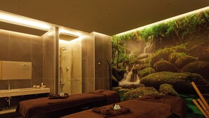 Un cuarto de spa con dos camillas de masaje, un lavamanos y un mural de una cascada.