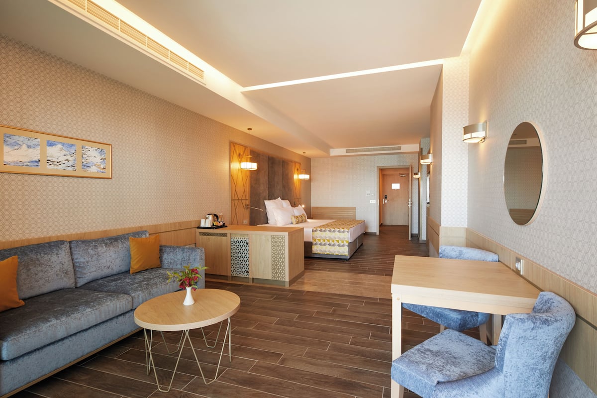 Une chambre d’hôtel moderne comprenant un canapé, une petite table ronde, un lit avec une tête de lit en bois et un coin repas avec une table et des chaises.