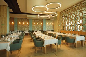 A restaurant with multiple tables, green chairs, and a geometric wall design. - Secrets Sunny Beach Resort & Spa (Nessebar)
