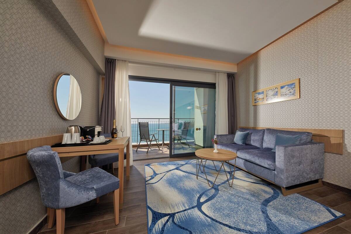 Une chambre d’hôtel moderne dotée d’un balcon, d’un canapé, d’un bureau avec une chaise et d’une table basse.