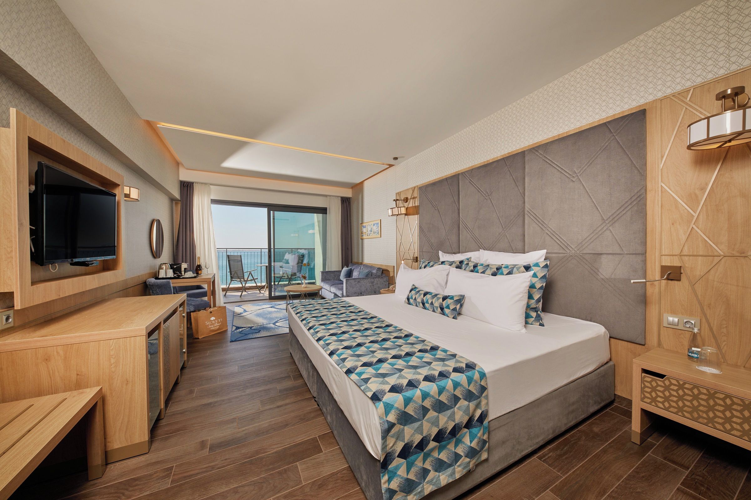A modern hotel room with a large bed, a TV, a desk, and a balcony with a city view.