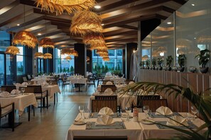 A restaurant with tables set for dining, large windows, and hanging light fixtures. - Secrets Sunny Beach Resort & Spa (Nessebar)