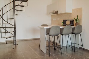 A modern kitchen with a white countertop, four grey chairs, a black metal spiral staircase, and a potted plant on the counter. - River View Boutiques Apts (Ayia Napa)