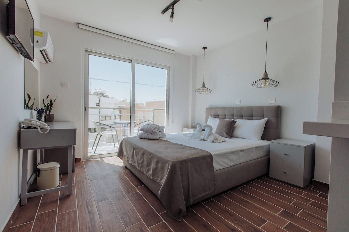 Quarto moderno com uma cama grande, mesas de cabeceira, uma escrivaninha com telefone e uma porta de vidro deslizante para área externa.