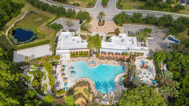Eine Vogelperspektive zeigt ein Resort mit einem großen Schwimmbecken, Palmen und einem Parkplatz.