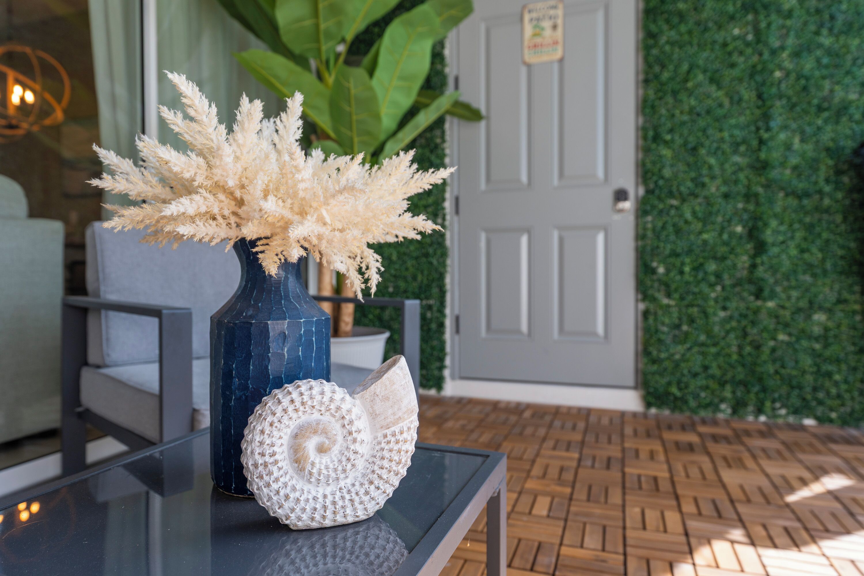 Una mesa con un jarrón de flores secas, una concha decorativa y una planta en maceta.