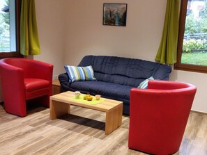 A room with a dark blue sofa, two red armchairs, a wooden coffee table, and a painting on the wall. - Schweizer, Obersaxen-Affeier, (Obersaxen), 34006B by Interhome (Obersaxen Affeier)