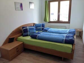 A single bed with a wooden headboard, a bedside table, and a window with a view of the outside. - Schweizer, Obersaxen-Affeier, (Obersaxen), 34006B by Interhome (Obersaxen Affeier)