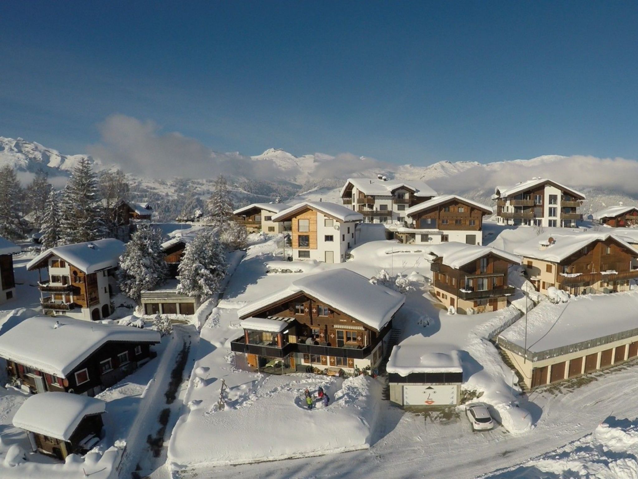 Ein verschneites Dorf mit mehreren Chalets, blauem Himmel und einer Bergkulisse.