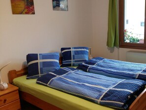A single bed with blue bedding, a bedside table, a lamp, and a window with a view of greenery. - Schweizer, Obersaxen-Affeier, (Obersaxen), 34006B by Interhome (Obersaxen Affeier)