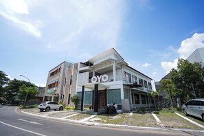 Un edificio con un llamativo letrero 'OYO', un acceso cubierto y un estacionamiento con coches.