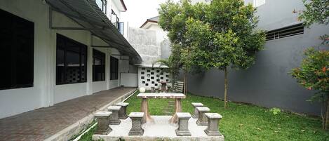 Un pati amb una taula d'escacs, bancs de pedra i un arbre petit.