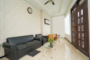Una habitación con un sofá de cuero negro, una mesa de centro de vidrio con una planta, un escritorio de madera y una puerta con paneles de vidrio.