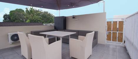 An outdoor patio with a table and chairs, a large umbrella, and an air conditioning unit.