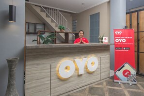 A reception desk with a large illuminated 'OYO' sign, a staircase in the background, and a promotional banner for the OYO app. - Irooms (Ngaglik)