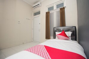 A hotel room with a bed, a window with curtains, an air conditioning unit, and a door. - Irooms (Ngaglik)
