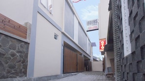 A narrow street with a building featuring a large wooden gate and a sign for 'iROOMS'. - Irooms (Ngaglik)