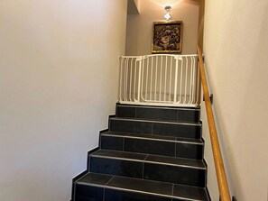 Eine Treppe mit schwarzen Stufen und einem weißen Geländer, die zu einer Zwischenebene mit einem gerahmten Kunstwerk führt.