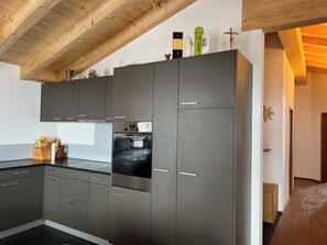 Eine moderne Küche mit grauen Schränken, einer Holzbalkendecke und einem eingebauten Backofen.