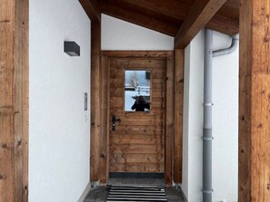 Une porte en bois avec une petite fenêtre, une poignée de porte en métal et un tuyau métallique qui longe le mur.