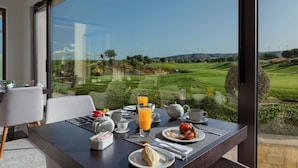 A dining table with breakfast items, a view of a golf course, and a large window.