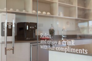 Cocina moderna con cafetera y puerta de vidrio que muestra un mensaje sobre disfrutar una bebida de cortesía.